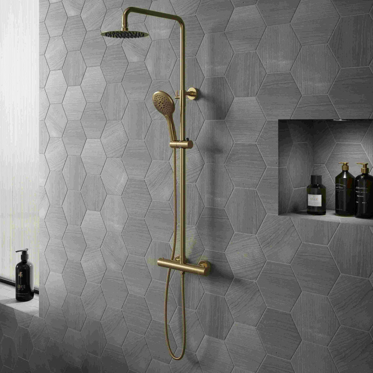 Bathroom with hexagonal gray tiles, gold shower fixtures, and shelves with bottles.
