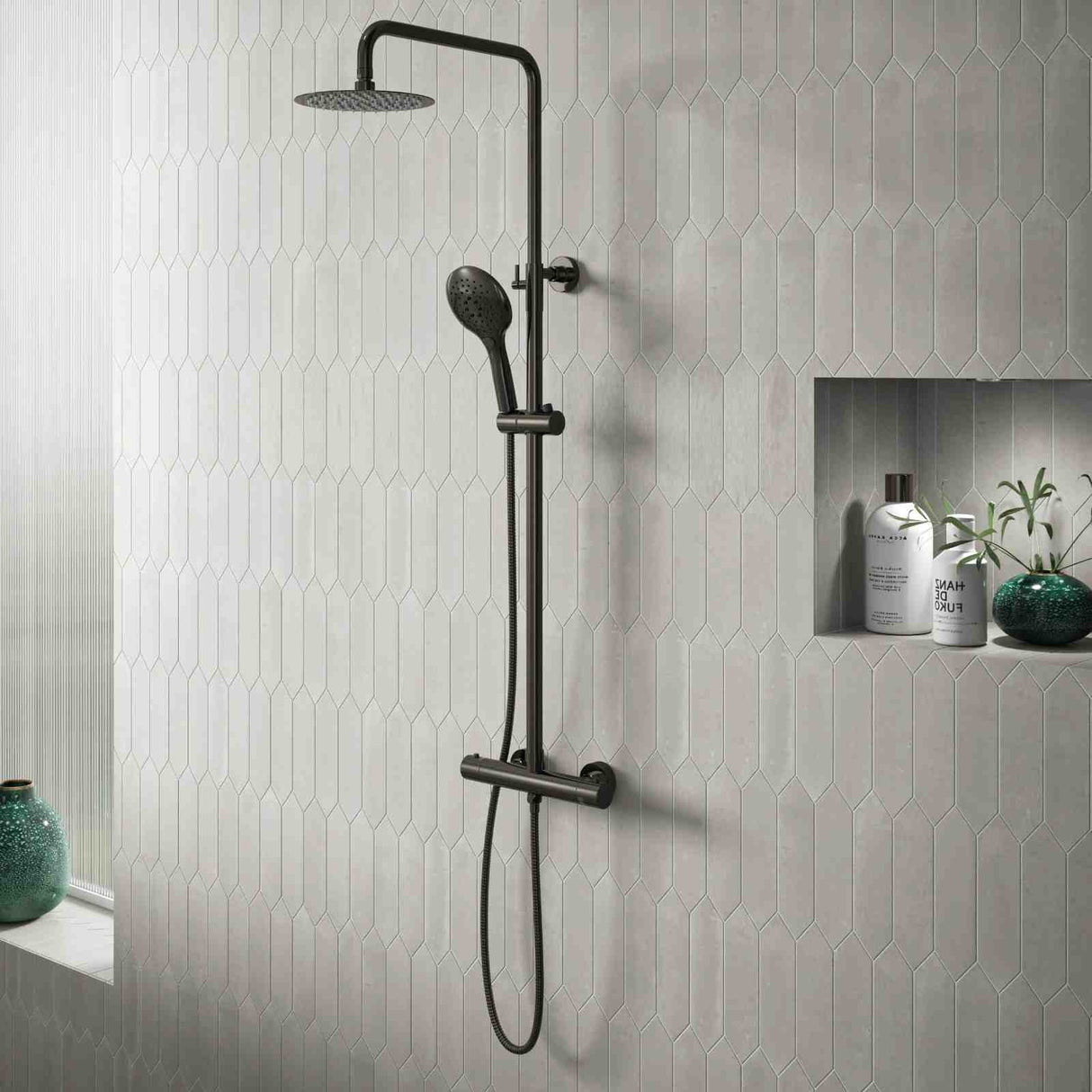 Black shower system mounted on a tiled wall with decorative elements.