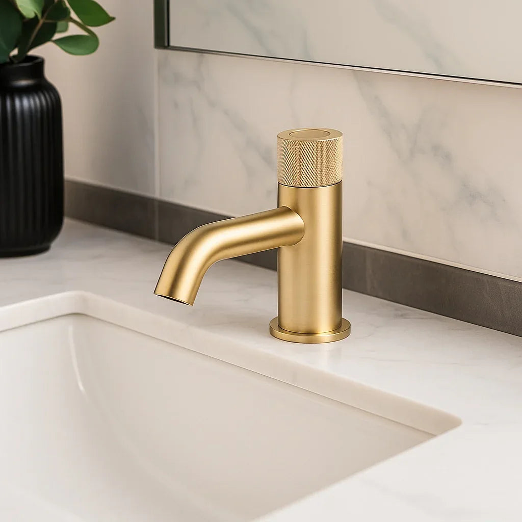 Gold faucet on a bathroom sink with a marble wall in the background