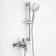 Chrome shower head and control handle set against a white tiled wall.