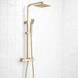 Gold shower system with square rain shower head and handheld shower on a white tiled wall.