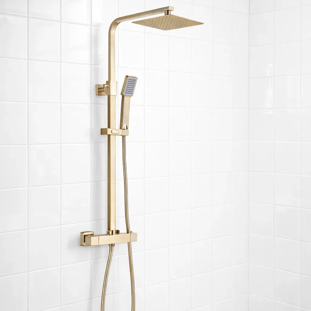 Gold shower system with square rain shower head and handheld shower on a white tiled wall.