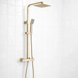 Gold shower system with square rain shower head and handheld shower on a white tiled wall.