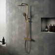 Bathroom with hexagonal gray tiles, gold shower head and hose, and shelves with bottles.