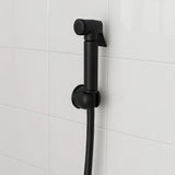Black shower head and hose against a white tiled wall