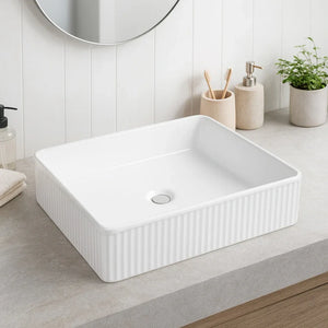 White rectangular sink in a bathroom setting with a mirror, soap dispenser, and plant.