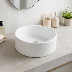 White ceramic sink on a bathroom counter with toiletries and plants.