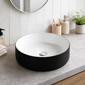 Black and white round sink on a bathroom counter with toiletries and a mirror.