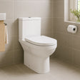 White toilet in a bathroom with beige tiles and a window.