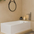 Modern bathroom with a white bathtub, candle, and bottles on a beige countertop.