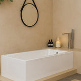 Modern bathroom with a white bathtub, candle, and bottles on a beige countertop.