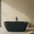 Modern black freestanding bathtub in a minimalistic bathroom with beige walls and floor.