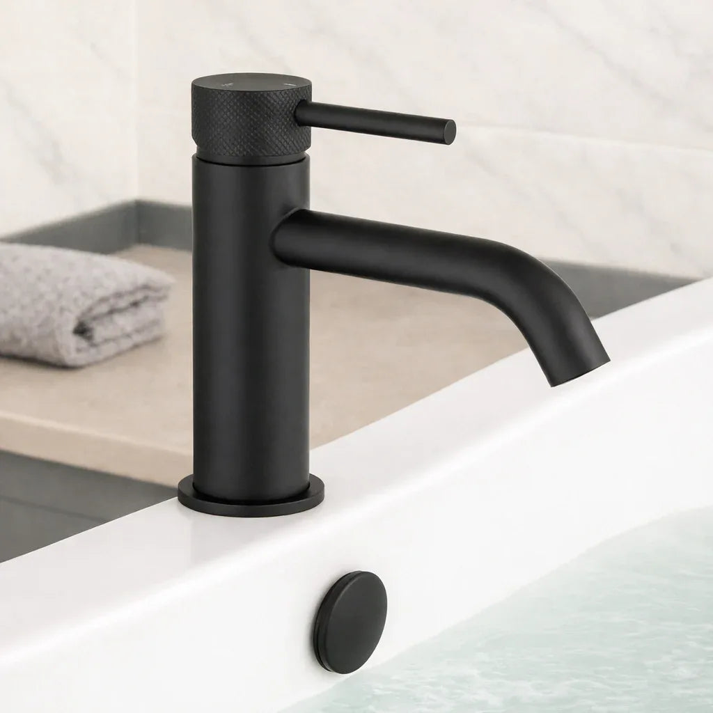 Black faucet on a bathroom sink with a towel in the background