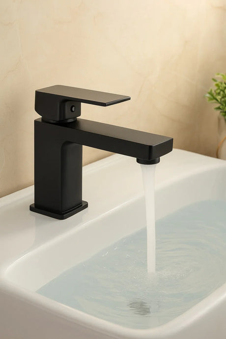 Black faucet on a sink with water flowing, against a beige wall.