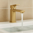Gold faucet with water flowing into a sink against a beige tiled wall.