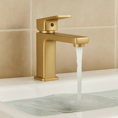 Gold faucet with water flowing into a sink against a beige tiled wall.