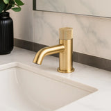 Gold faucet on a bathroom sink with a marble wall in the background
