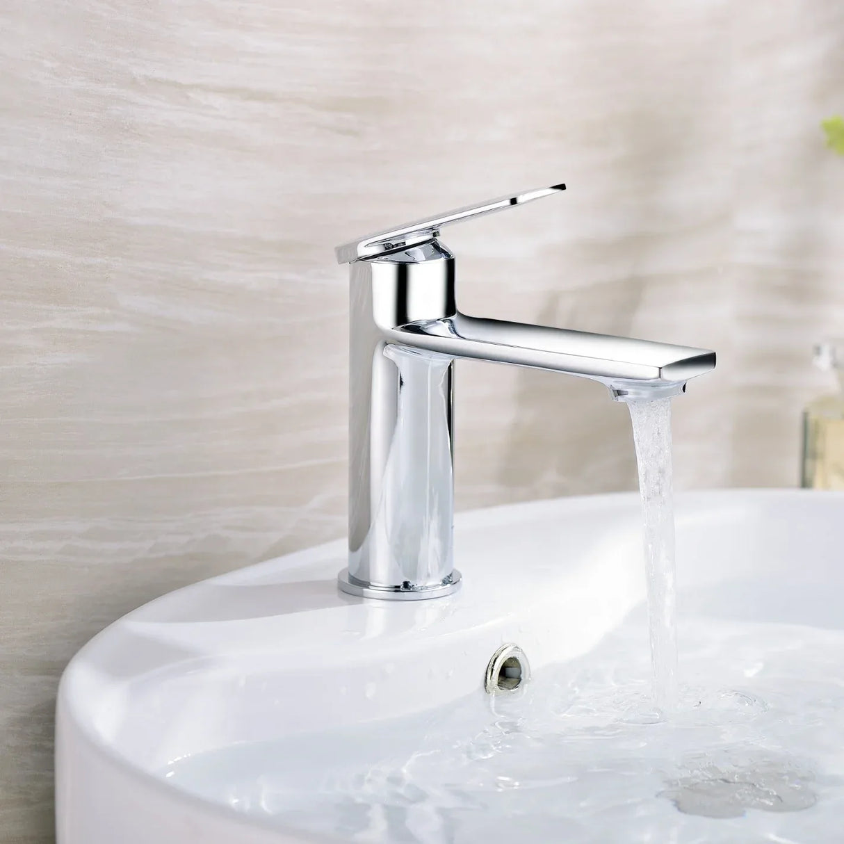 Chrome faucet on a white sink with water flowing, against a neutral wall.