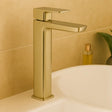 Gold faucet on a bathroom sink with a beige tiled wall in the background